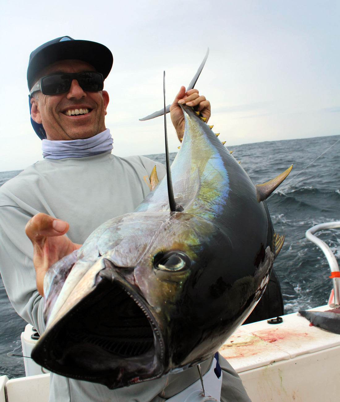 Man holding a large fish on a boat with ocean in the background