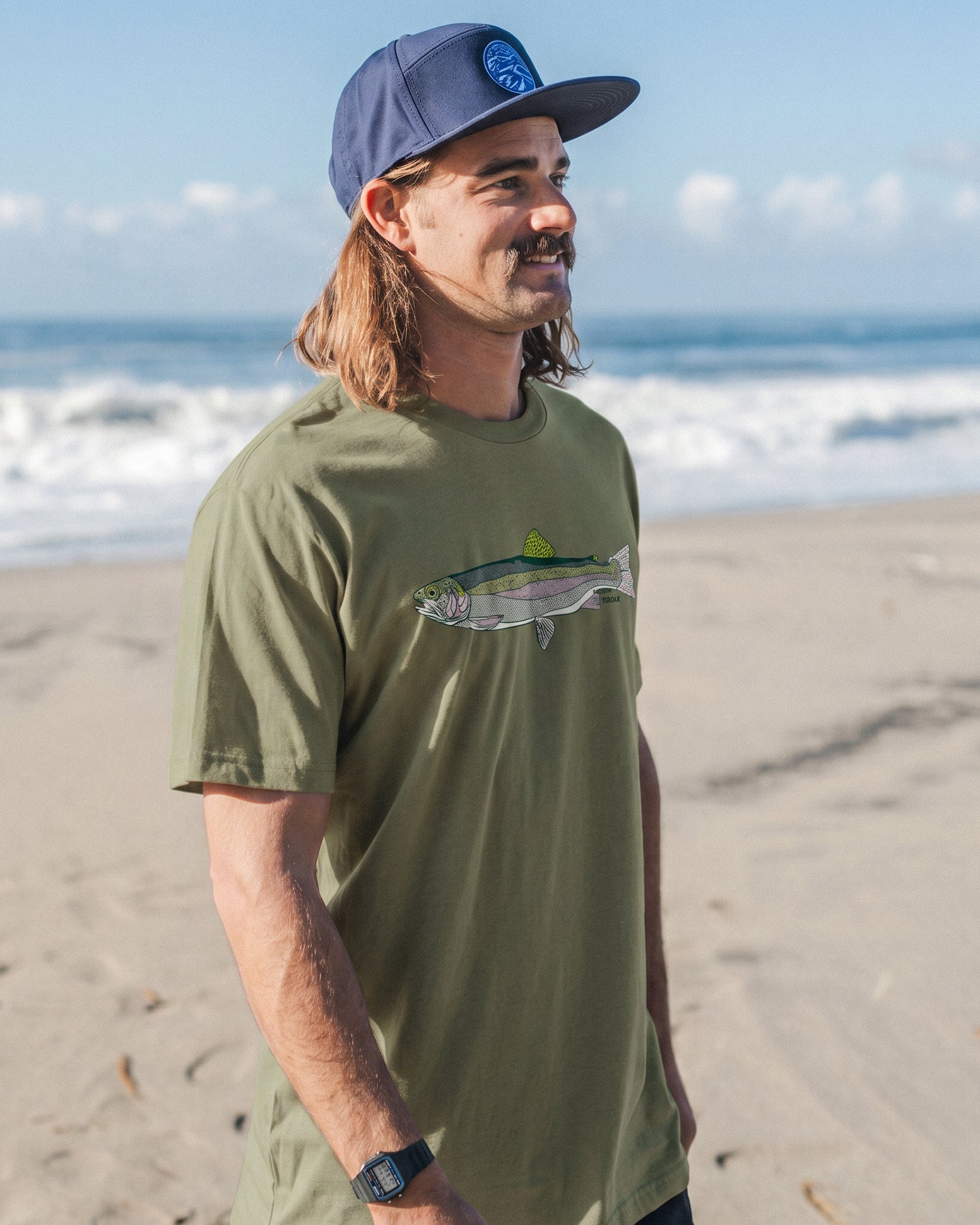 Man wearing a green t-shirt with a trout design on a beach
