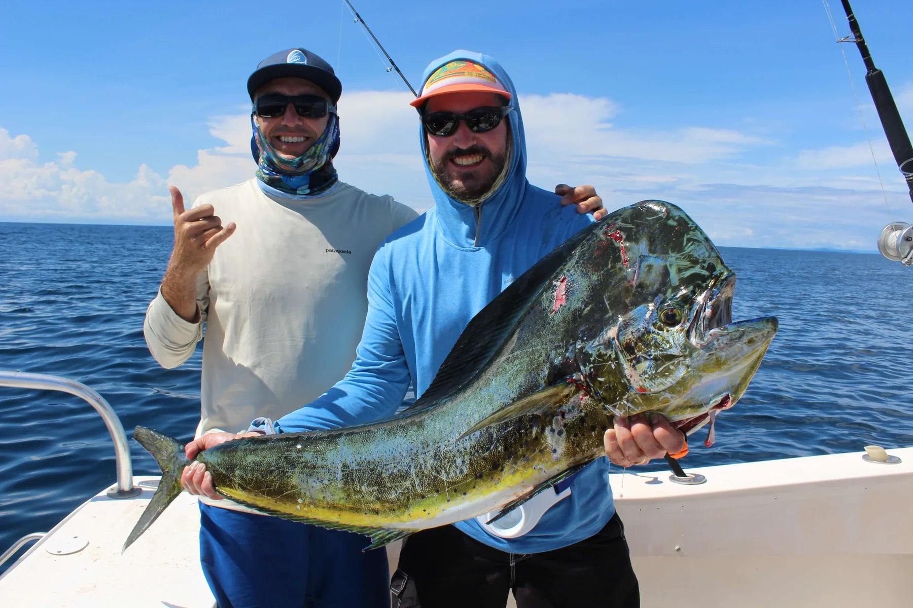 Two men on a boat holding a large fish with a clear blue sky and ocean background.