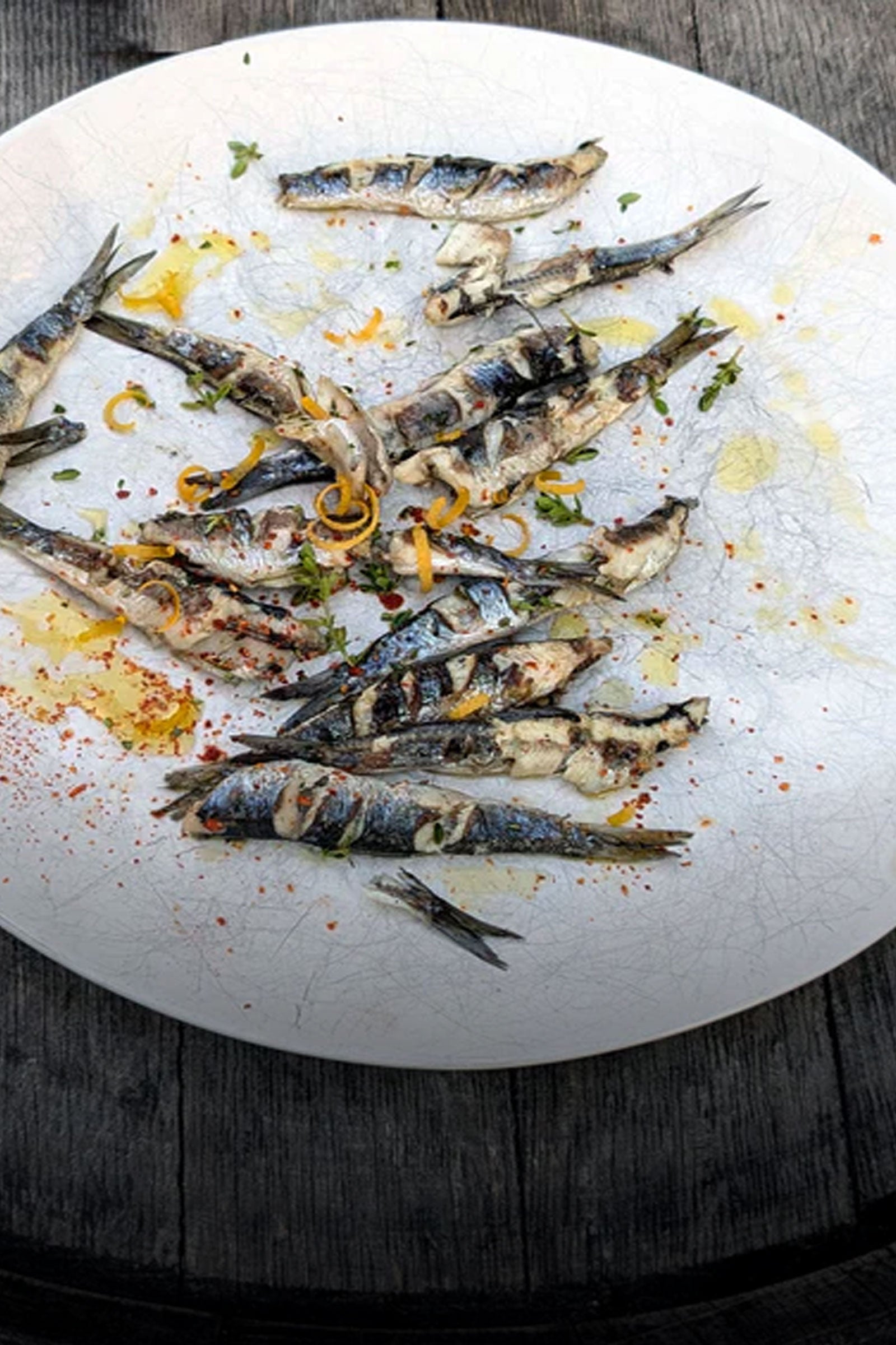 Grilled anchovies on a white plate with garnishes on a wooden surface