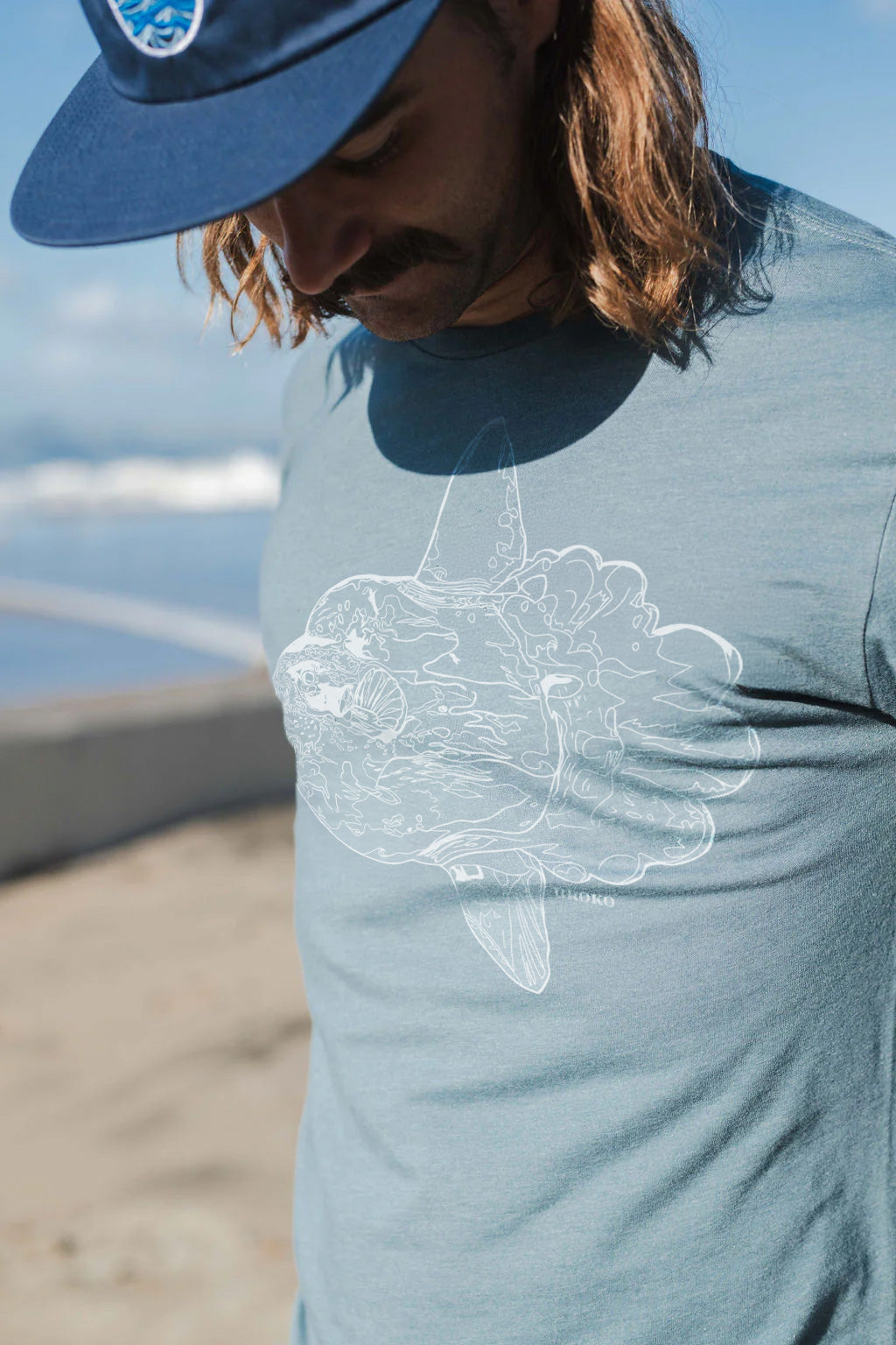 Person wearing a blue t-shirt with a mola mola design at the beach