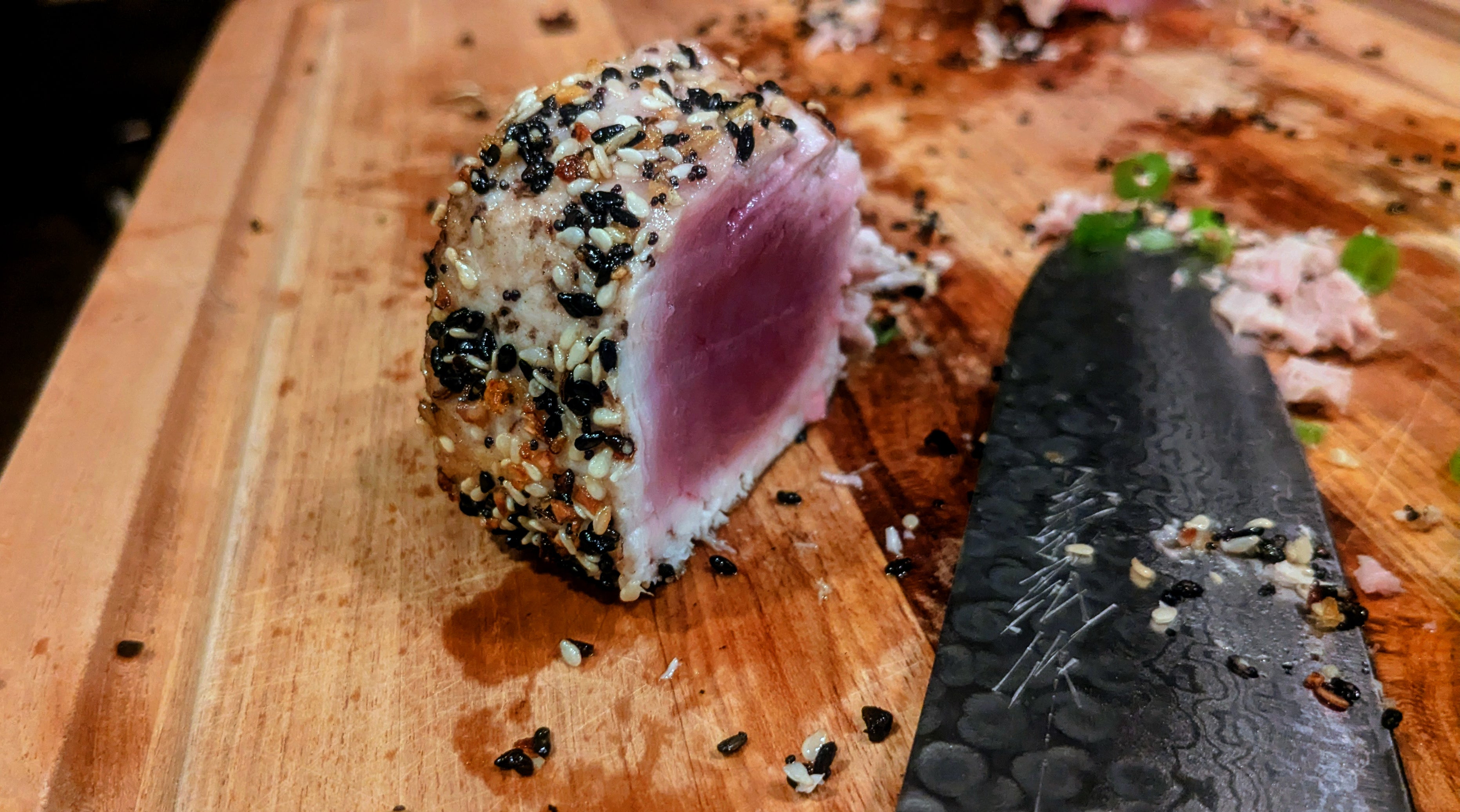 Sliced tuna with sesame seeds on a wooden cutting board with a knife.